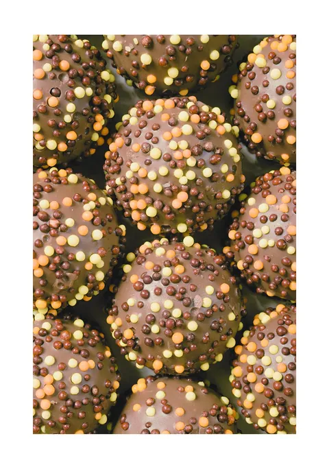 Close-up van ronde chocoladebonbons versierd met gele en oranje suikerparels.