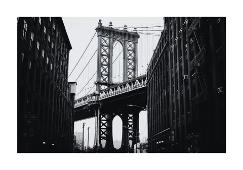 Zwart-witfoto van de Manhattan Bridge gezien tussen twee bakstenen gebouwen in New York.
