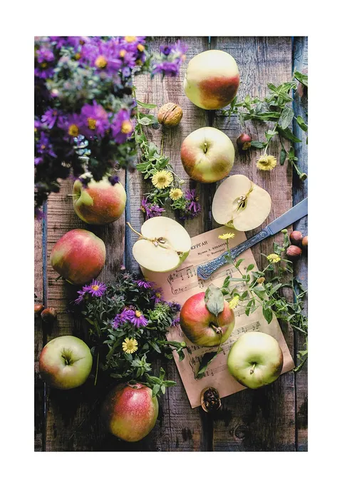 Bovenaanzicht van appels, paarse bloemen en bladmuziek op een rustieke houten tafel.