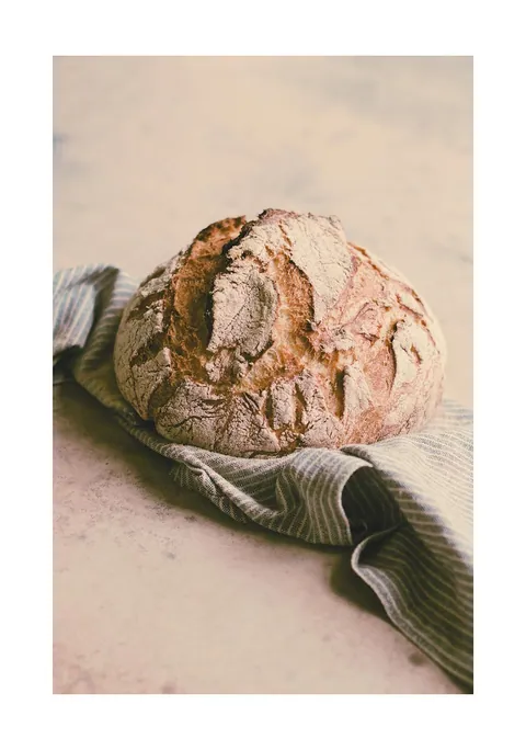 Rond ambachtelijk gebakken brood op een gestreepte theedoek op een lichte ondergrond