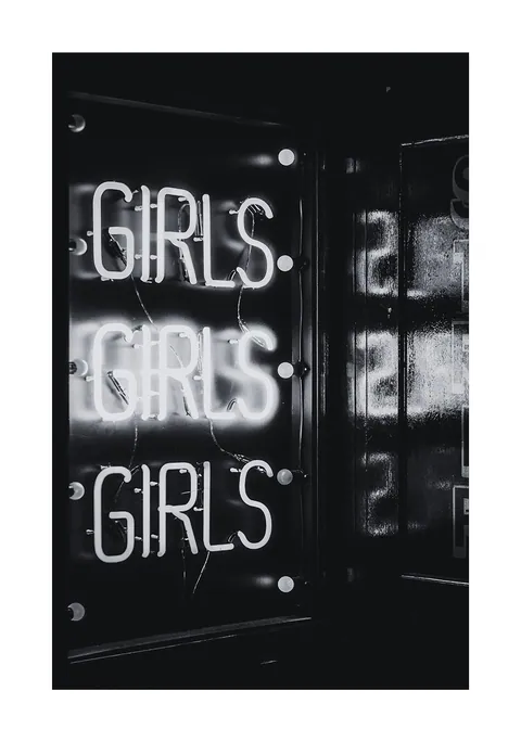 Zwart-witfoto van een verlicht neonbord met driemaal het woord Girls onder elkaar.