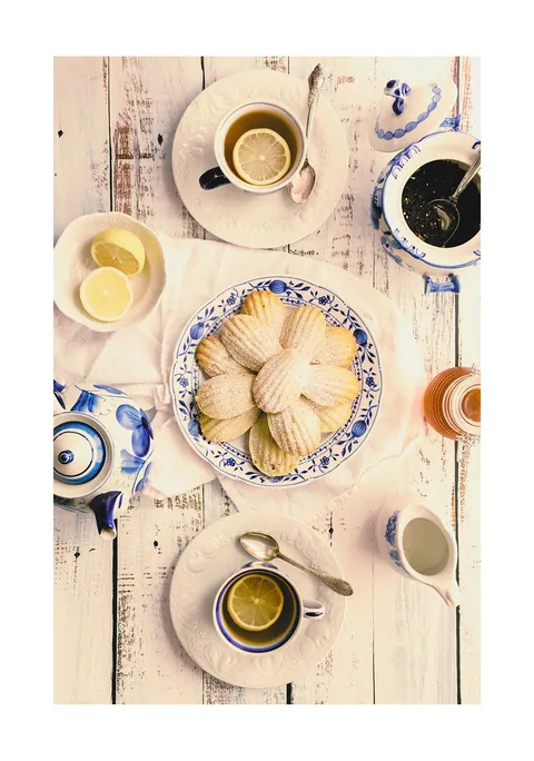 Bovenaanzicht van een theetafel met blauw-wit servies, citroenthee en madeleines