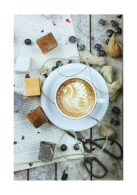 Bovenaanzicht van een kop cappuccino met latte art, fudge, bessen en een vintage schaar.