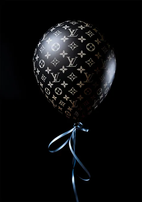 Zwarte ballon met goudkleurig monogrampatroon en blauw lint tegen een zwarte achtergrond.