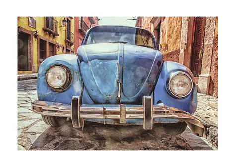 Een verweerde blauwe vintage auto geparkeerd in een historische straat met kasseien