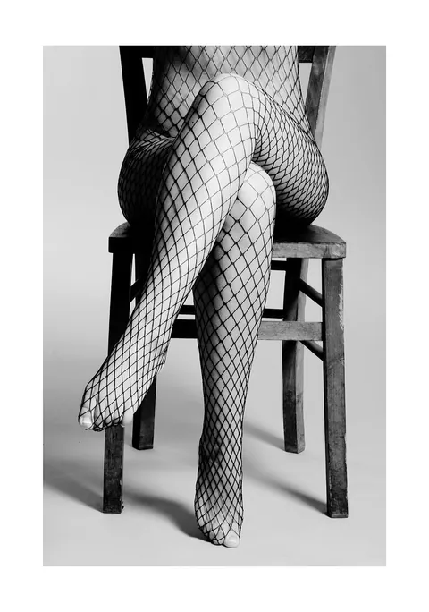 Zwart-wit foto van benen in visnetpanty op een houten stoel