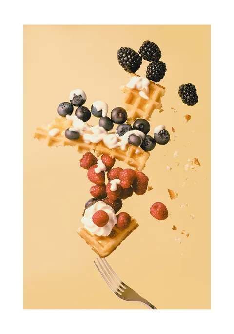 Zwevende stukjes wafel op een vork met bessen, frambozen en slagroom.